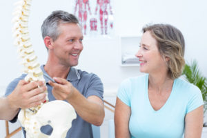Physiotherapist showing spine model to his patient in medical office